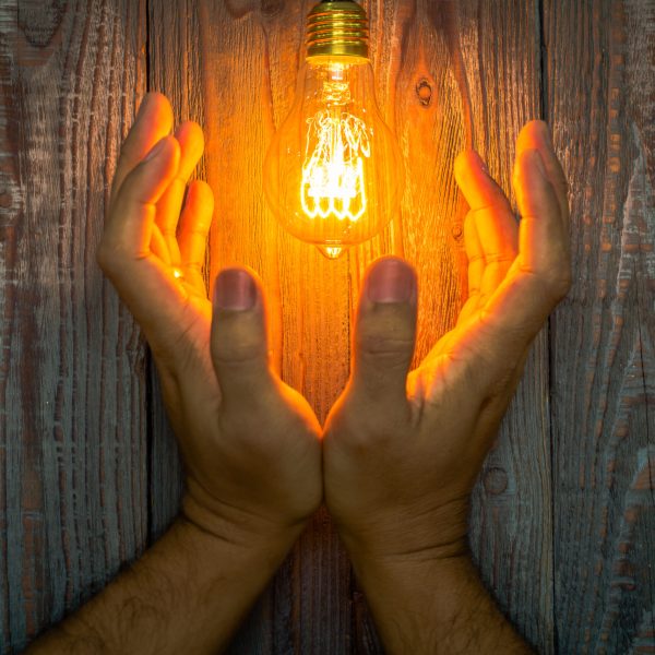 Hand with Glowing bulb on the wood background