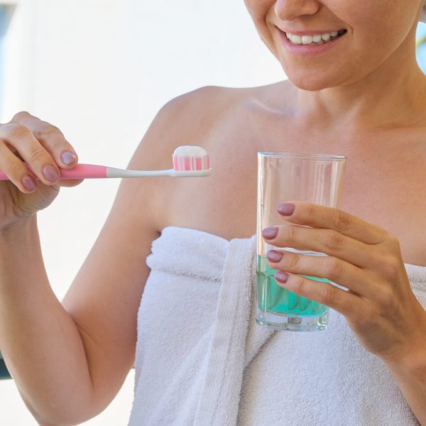Mature woman brushes her teeth, female with toothbrush glass of water