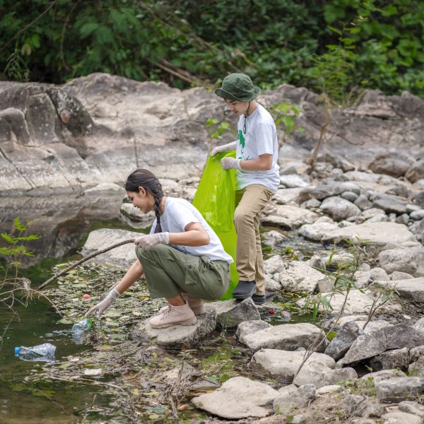 Volunteer Asian and children are collecting plastic bottles that flow through the stream into garbage bags to reduce global warming and environmental pollution. Volunteering and recycling concept.