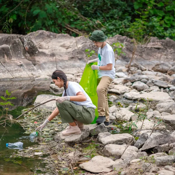 Volunteer Asian and children are collecting plastic bottles that flow through the stream into garbage bags to reduce global warming and environmental pollution. Volunteering and recycling concept.