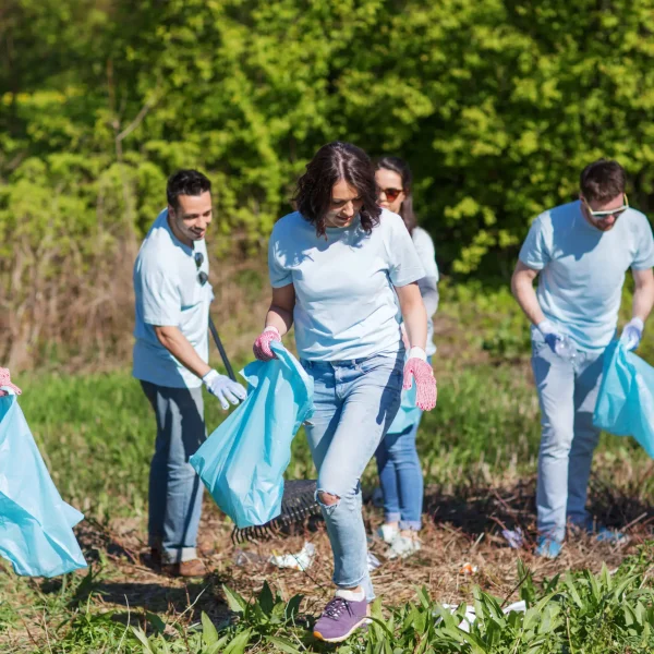 volunteering, charity, cleaning, people and ecology concept - group of happy volunteers with garbage bags cleaning area in park